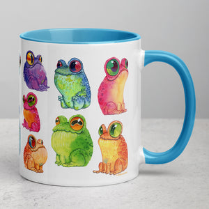 A colorful ceramic coffee mug with a blue handle featuring a collection of whimsical, vibrant frogs in various poses inspired by Chris Ryniak watercolor frog paintings from Bindlewood Shop's Frog Frenzy Mug.
