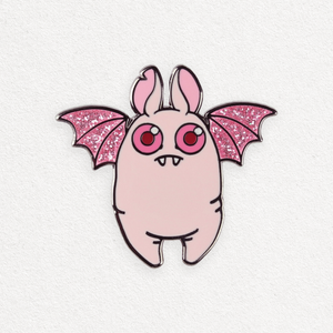 Illustration of a whimsical creature resembling a pink rabbit with bat wings, featuring the Bindlewood Shop Glittery Albino Bat Pin with sparkly pink glitter wings and large, round red eyes. The background is a simple, textured white.