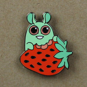 An Strawberry Bunny Pin designed by Amanda Louise Spayd, featuring a cute, cartoon-style character combining a green bunny and a red strawberry, set against a beige background. The bunny has large eyes and a

Brand Name: Bindlewood Shop