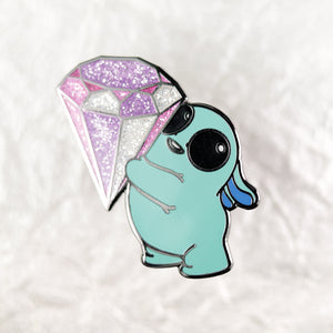 A cute Topaz Enamel Pin from Bindlewood Shop featuring a cartoon-style turquoise turtle peeking from underneath a glittery purple and silver diamond-shaped crystal jewelry, set against a soft white background.