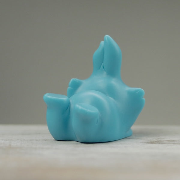 A small, smooth, blue sculpture of a playful animal lying on its back with its legs in the air, crafted by Chris Ryniak. Placed on a wooden surface against a plain grey background, this opaque resin figure features soft contours and minimal detailing.

Product Name: Robin's Egg Blue Bugbite
Brand Name: Chris Ryniak