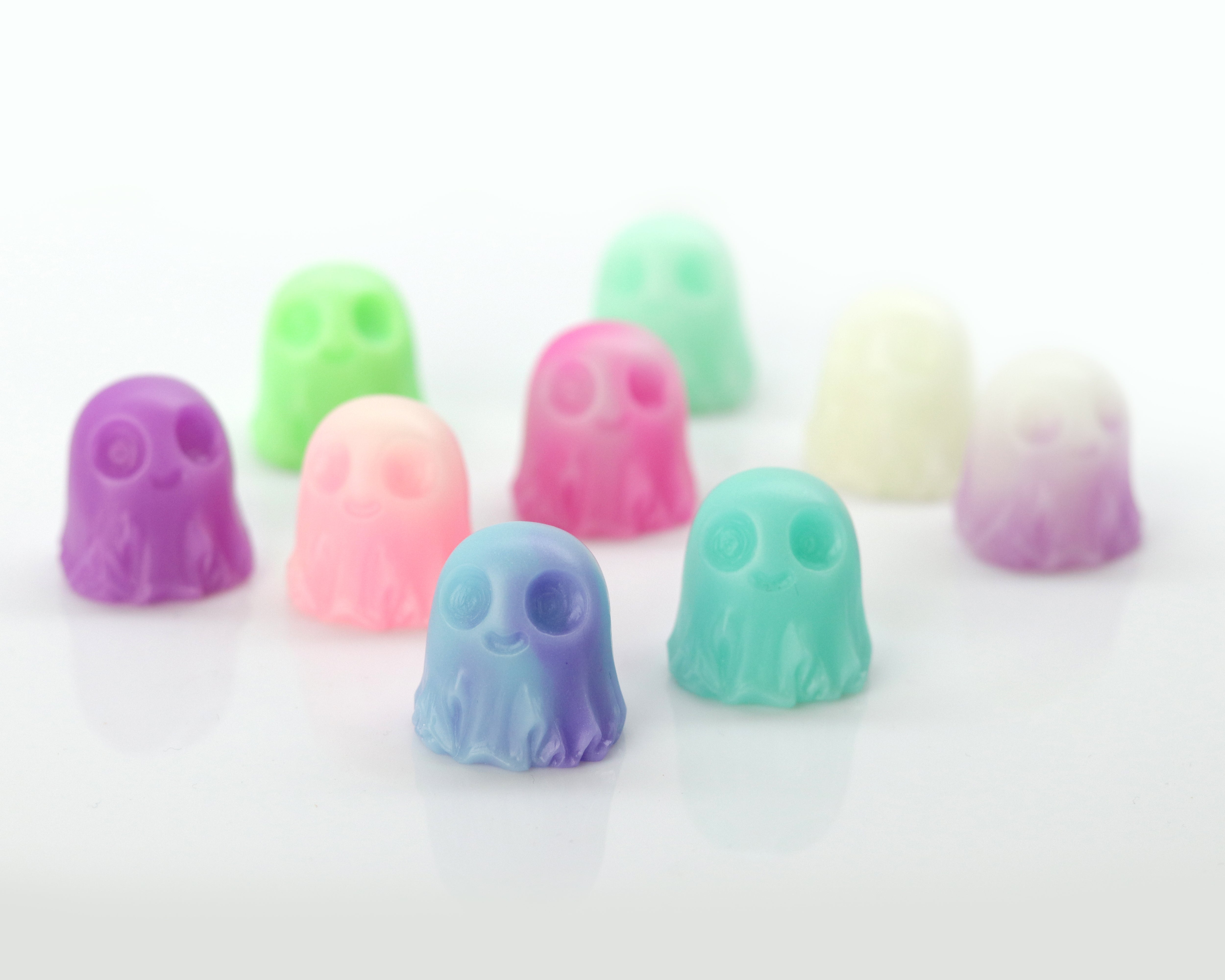 A selection of Giddy Ghost Glow 2-pack figurines from Bindlewood Shop—adorable, pastel-hued ghosts with big eyes—are displayed in neat rows on a white background. Available in shades of purple, blue, pink, green, and white, these figures sport cheerful expressions and some even glow in the dark.