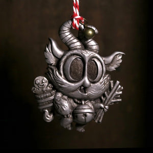 The Bindlewood Shop's Silver Lil' Krampus Ornament is a whimsical, small resin decoration with big eyes, horns, and pointed ears. Hand-painted, it holds a basket with a gingerbread figure and sticks. It hangs from a red-and-white patterned string against a dark background.