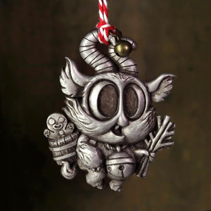 The Silver Lil' Krampus Ornament by Bindlewood Shop features a whimsical, hand-painted resin creature with large eyes, a curled horn, wings, and a bell. It carries a gingerbread figure and sticks in its basket. Hanging from a red and white string with an attached bell, it's truly festive.