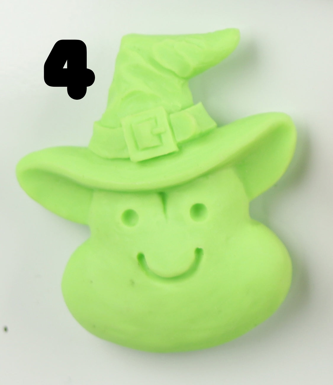 A light green, smiling cartoon witch face with a pointed hat and bold black number 4 on top left. Hand-sculpted Halloween Magnet by Bindlewood Shop—perfect for magnet collectors.
