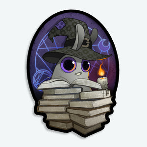 The Mystical Witchbunny Sticker (3-inch) from Bindlewood Shop features a cartoon rabbit in a wizard hat, reading by candlelight behind books with magical symbols. This waterproof matte vinyl sticker adds witchy charm anywhere you stick it!.