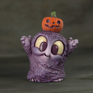 A Purple Pumpkin Patch Smurk from Chris Ryniak's collection stands with its arms raised, featuring wide eyes and a fluffy texture that add charm. The whimsical resin figure dons a tiny jack-o'-lantern on its head, perfectly set against a soft, dark background.