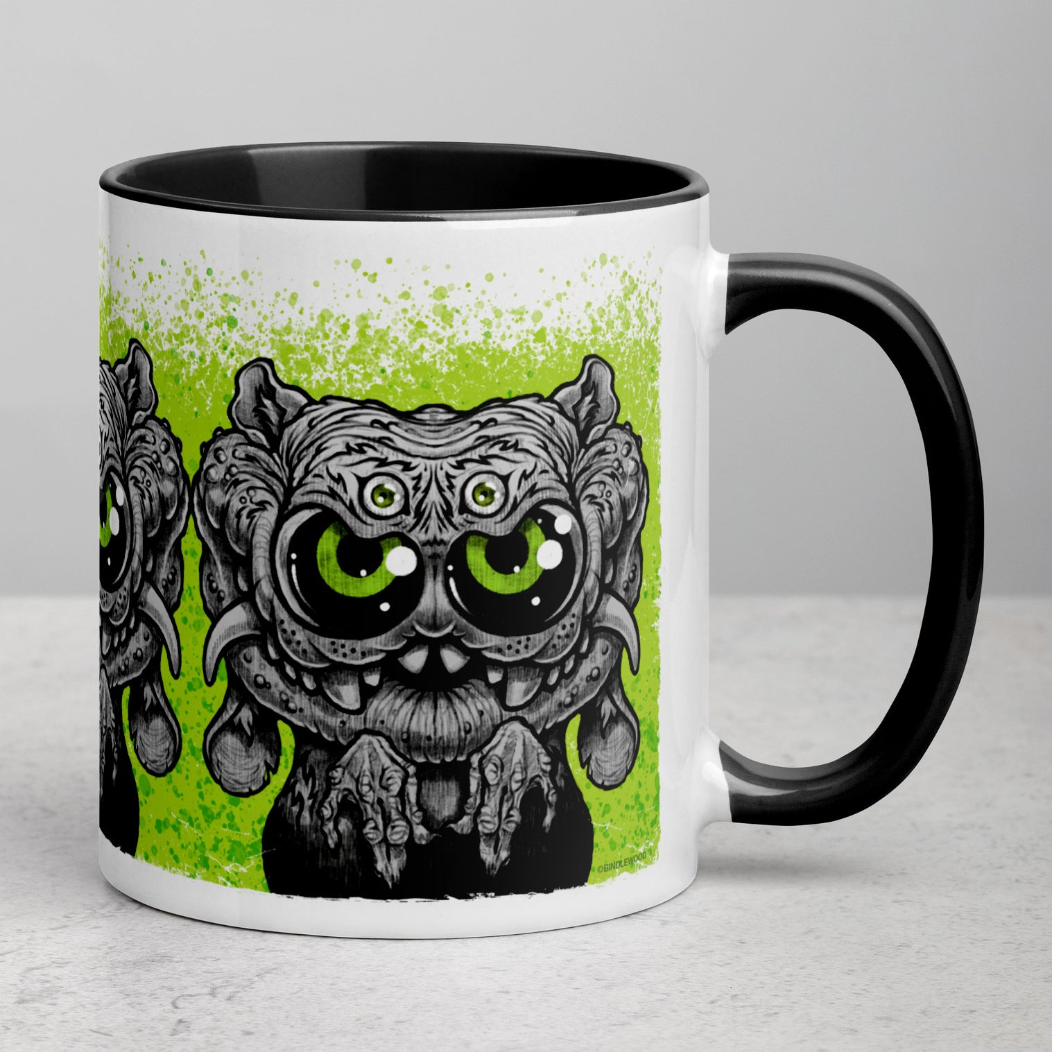 Introducing the Eyegurr Mug from Bindlewood Shop—a white ceramic mug with a black handle, showcasing an illustration of a wide-eyed, four-eyed creature sporting large green eyes and claws against a splattered green background. Perfect for collectors, this design captures the whimsical charm of Chris Ryniak’s signature monster mugs.