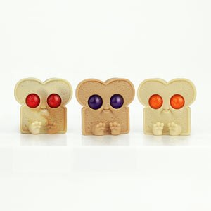 The Jammin' Jelly Toastboy blind-bag collectibles by Chris Ryniak feature three charming bread slice toys with big colorful eyes—red, purple, and orange—and intricately sculpted small hands and feet against a plain white background.