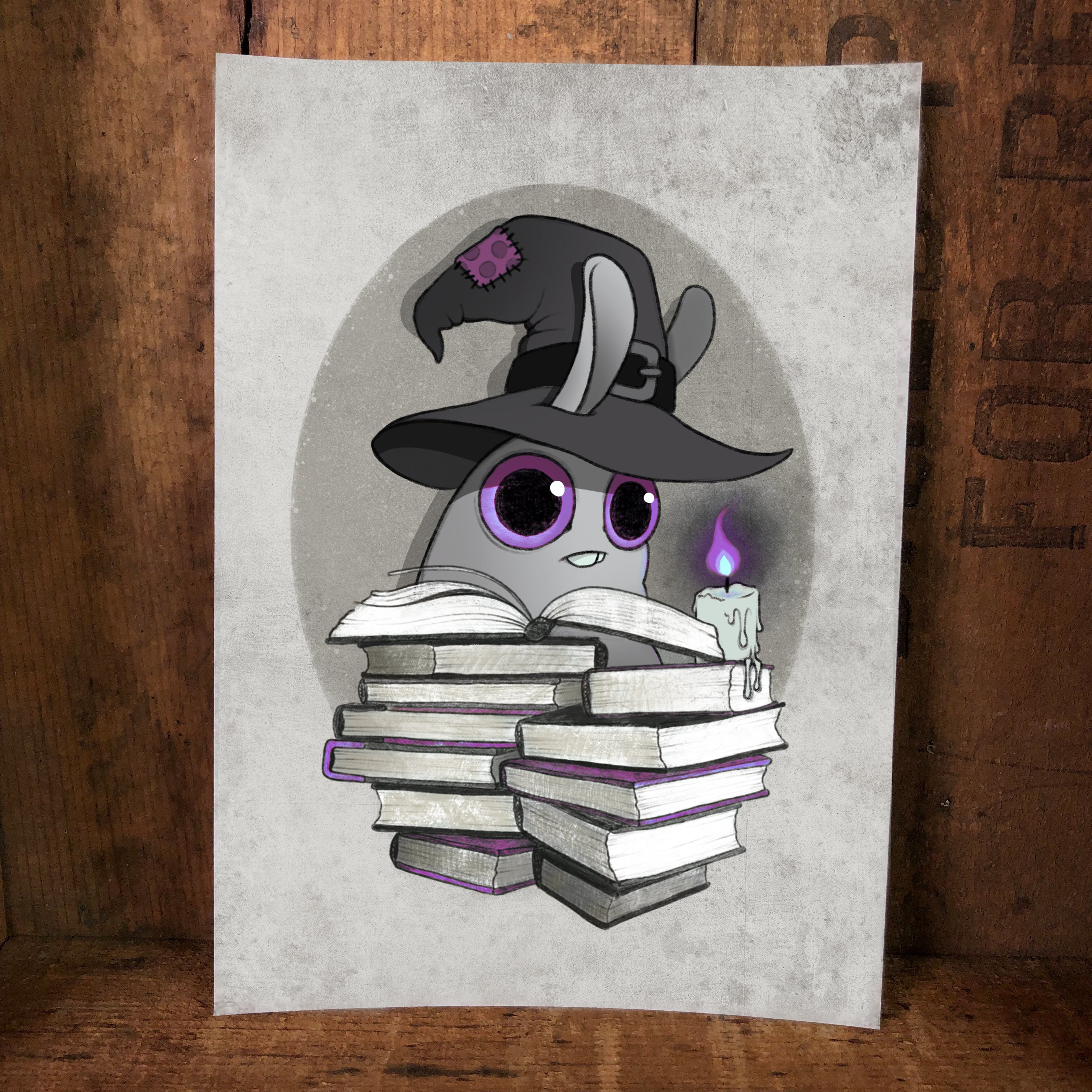 The "Witchbunny" print by Amanda L Spayd features a cute cartoon bunny in a witch hat with books and a purple-flame candle, set against a gray background with wood texture—perfect for archival paper fine art display.
