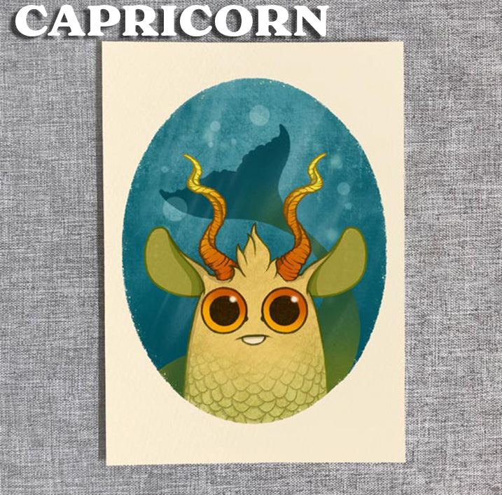 A cute cartoon creature with big brown eyes, green fish scales, horns, and green ears sits in an oval frame. "Capricorn" tops this Zodiac Prints by Amanda Louise Spayd, available from Bindlewood Shop—perfect for any art collection.