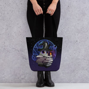 A person in black pants and boots holds the Neon Witchbunny Tote from Bindlewood Shop, featuring a cute cat with a wizard hat sitting on books, with a magic circle and crescent moon behind it.