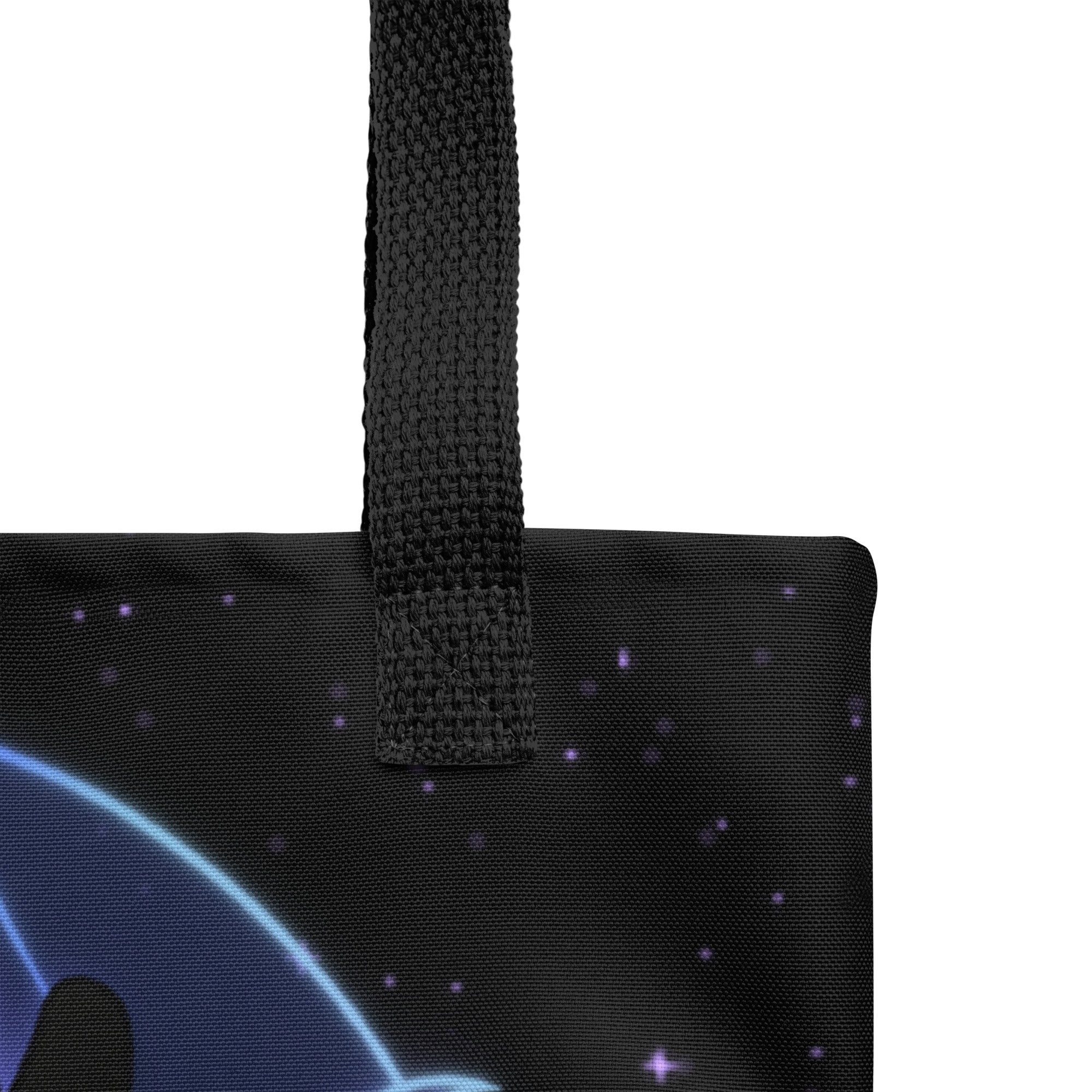 Close-up of the Mystical Witchbunny Tote by Bindlewood Shop, a black bag with woven handle, featuring a blue and purple starry night sky design and a curved shape in the lower left corner.