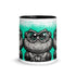 The Tode Mug by Bindlewood Shop is a white ceramic mug with a black interior, showcasing a bold, cartoon-style frog with large eyes and textured skin set against a turquoise background in a mirrored, repeated pattern—an ideal collectible art mug for enthusiasts of whimsical design.