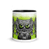 Introducing the Eyegurr Mug from Bindlewood Shop—a white ceramic mug with a sleek black interior, showcasing a detailed, cartoonish three-eyed creature with vibrant green eyes and sharp fangs set against a bold green splatter background. Ideal for collectors and fans of unique drinkware, this design draws inspiration from the whimsical artistry of Chris Ryniak monster mugs and features the initials “SMR” at the bottom center.
