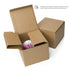 An open brown cardboard box with a white and pink Radbit Mug from Bindlewood Shop inside sits next to a closed box. Text reads: “Packages vary based on delivery location, but we ensure that the product—like this Radbit Mug—is well protected.”.