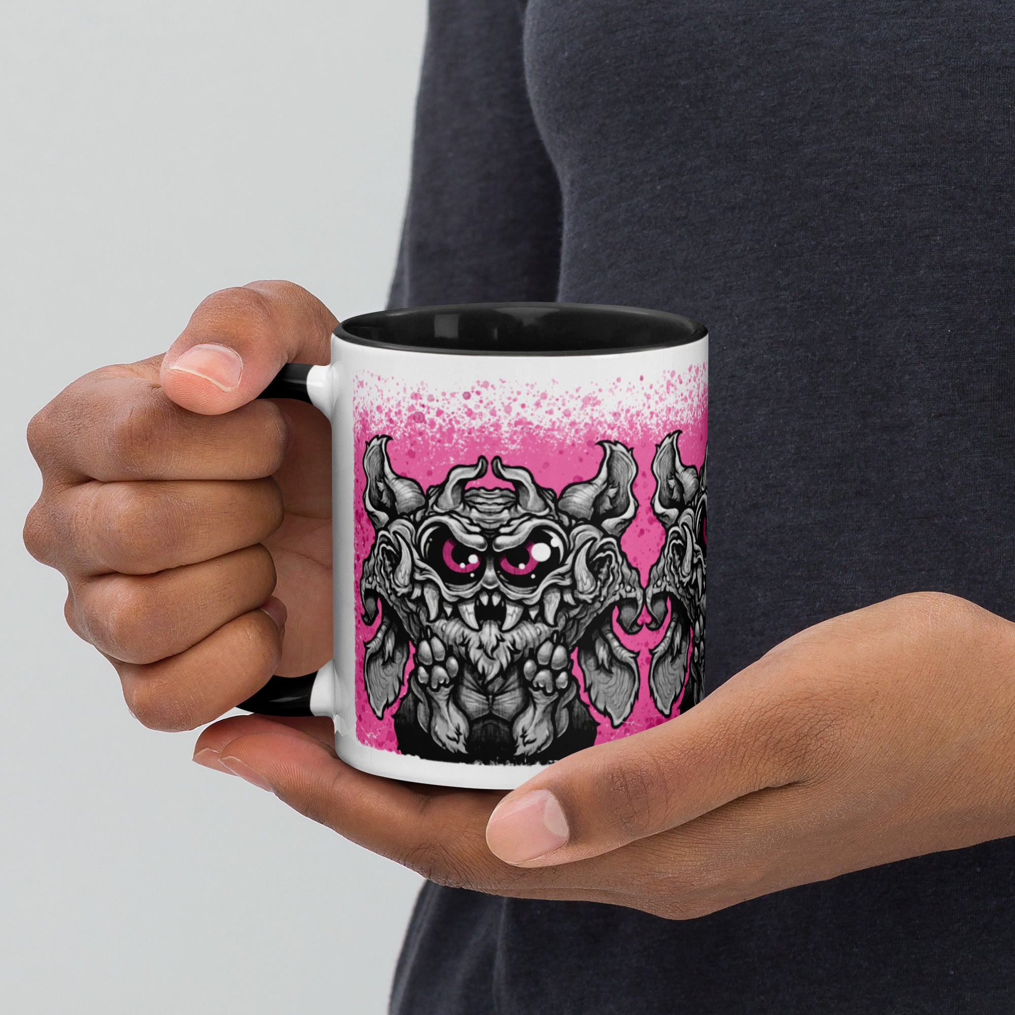A person holds a black and white Radbit Mug by Bindlewood Shop, featuring a cartoonish, fierce bat-like creature design against a pink background.