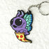 The Mothpup Keychain from Bindlewood Shop is a cute PVC rubber accessory featuring the purple cartoon bug from Thimblestump Hollow with big eyes and blue-green wings, riding a slice of pepperoni pizza on a textured white background.