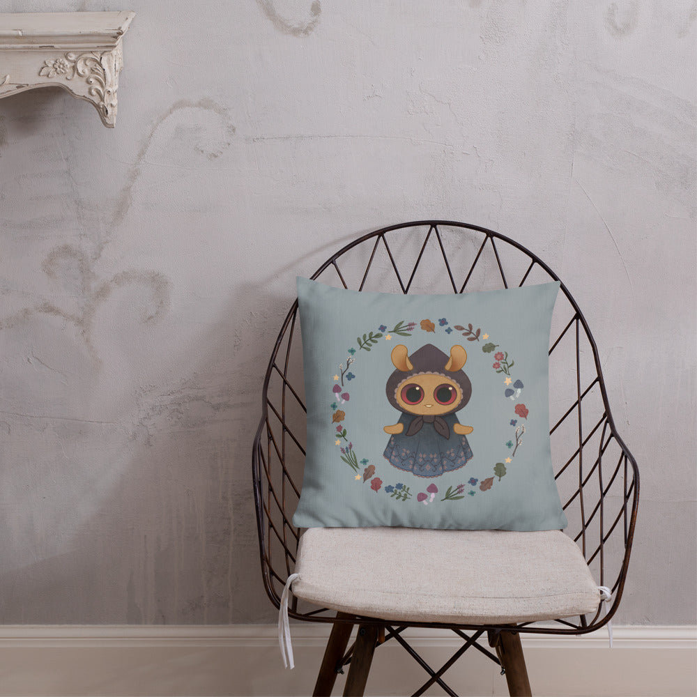 A metal wire chair with a cushioned seat features the charming Twilight Sprite Throw Pillow from Bindlewood Shop, adorned with an illustration of a cute bear wearing a dress, framed by a wreath of colorful flowers against a light blue background. The chair sits in a simply decorated room, evoking cottagecore interior design charm.