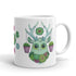 The Succulent Mug by Bindlewood Shop is a whimsical ceramic mug that showcases a cute green creature adorned with large eyes and branch-like antlers. It features an array of succulents and flowers, with pink pots hanging from its antlers, offering a delightful and colorful design that is both charming and dishwasher safe.